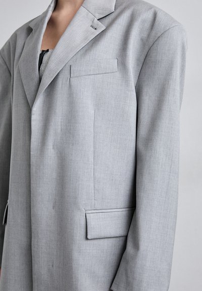 Vaaleanharmaa blazer, jossa on lovellinen kaulus, yksittäinen rintatasku ja sivutaskut. Kankaassa on hienovarainen tekstuuri ja se on muotoiltu hyvin istuvaksi.