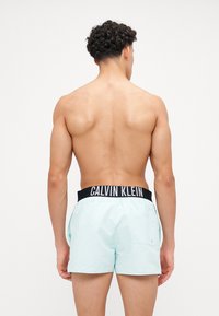 Svetlo modri kopalni šortai z črnim pasom Calvin Klein, izdelani iz gladkega materiala, s posamezno zadnjo žepom in sproščenim krojem.