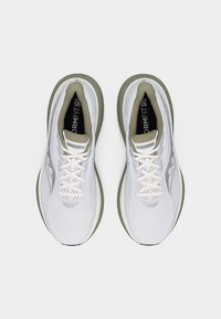 Ζεύγος λευκών και μπεζ παπουτσιών τρεξίματος Saucony, φωτογραφημένα από πάνω, με κορδόνια και μαλακές σόλες σε απλό φόντο.