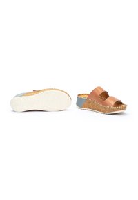 Zapatos de cuero marrón tipo slip-on con dos correas anchas, que cuentan con una suela de corcho y un acento en el talón de color azul claro. La parte inferior tiene un grip de goma blanca texturizada.