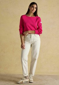 Vaaleanpunaisiraidallinen pitkähihaine paita, joka on yhdistetty korkeavyötäröisiin kermaisiin farkkuihin ja beigeihin tennareihin. Paidassa on käänneverkot ja vähäiset varusteet.