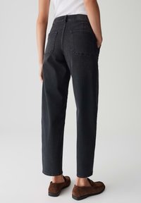 Jeans neri a vita alta con un design a gamba dritta, due tasche posteriori e una finitura testurizzata, abbinati a scarpe in suede marroni.