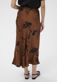 Jupe en satin marron avec motif floral noir, silhouette en A, longueur mi-mollet, texture lisse et légère évasement à l'ourlet.
