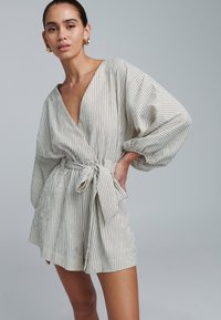 Stribet omslagskjole i lys beige og guld, med dyb V-hals, brede ærmer og bånd i taljen til justerbar pasform. Glat, tekstureret stof.