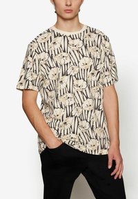 Gėlių raštų T-shirt kreminės spalvos su šviesiai rudomis ir juodomis juostelėmis. Turi trumpas rankoves, apvalią iškirptę ir laisvą kirpimą.