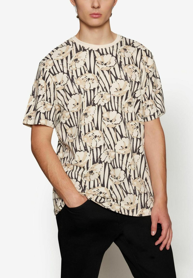 Gėlių raštų T-shirt kreminės spalvos su šviesiai rudomis ir juodomis juostelėmis. Turi trumpas rankoves, apvalią iškirptę ir laisvą kirpimą.