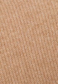 Gros plan sur un tissu en laine beige doux tricoté, avec une texture duveteuse et un motif de côtes verticales visible.