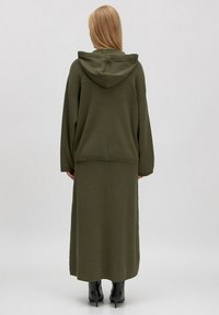 Olijfgroene hoodie met capuchon en bijpassende maxi rok, met een relaxte pasvorm en lange mouwen, gemaakt van zachte stof; gecombineerd met enkellaarsjes.