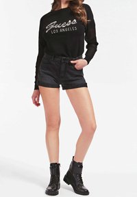 Zwart shirt met lange mouwen en "Guess Los Angeles" in pailletten, gecombineerd met donkere denimshorts en zwarte vetercombatlaarzen.