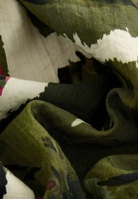 Tissu vert et beige avec une surface texturée et froissée, présentant un motif semblable à un camouflage agrémenté de touches de rose et d'accents blancs.
