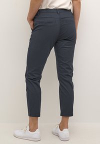 Pantalons chino ajustés bleu foncé avec une texture lisse, longueur raccourcie et deux poches arrière. Associés à des baskets blanches.