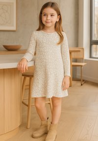 Langärmliges cremefarbenes Kleid mit floralem Muster, A-Linien-Form und weicher Textur, kombiniert mit sandfarbenen Ankle Boots. Einfaches und komfortables Design.