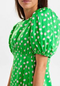 Zielona sukienka w różowe kropki, z bufkami i marszczonym pasem, wykonana z gładkiego, lekkiego materiału.