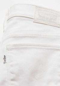 Witte denim jeans met een achterzak, voorzien van kenmerkende stiksels en een tan leren label met de opdruk "Levi Strauss & Co."