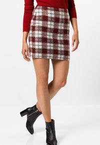 Mini-jupe à carreaux rouges et blancs en tissu doux, dotée d'une coupe près du corps et de poches latérales. Portée avec des bottines noires à la cheville.