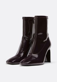 Stivaletti alla caviglia in vernice bordeaux con punta appuntita, tacco alto a blocco e chiusura con zip laterale. Texture liscia e design senza cuciture.