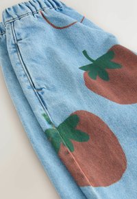 Lyseblå denimbukser med elastisk taljebånd, med et stort trykt jordbærmotiv i brun og grøn på benet.