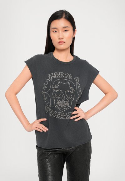 Zwart T-shirt met korte mouwen en een grafisch ontwerp van een schedel, met gestifte tekst. Zacht materiaal met een relaxte pasvorm. Model draagt het met zwarte, gestructureerde broek.