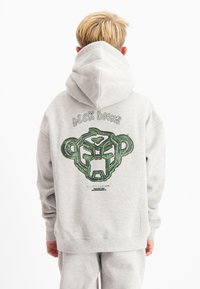 Grijze pullover hoodie met een grote groene afbeelding van een apenkop op de achterkant, met gedurfde omtrekken en gestileerde tekst erboven.