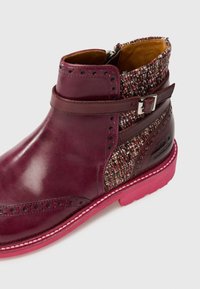 Bordo odinė aulinė avalynė su pintomis audinio detalėmis, sagties akcentu ir rožiniu guminio padu. Pasižymi brogue stiliaus perforacijomis.