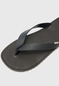 Sorte flip-flops med teksturerte stropper, flat gummisåle og minimale sømdetaljer. Materialet ser glatt og slitesterkt ut.