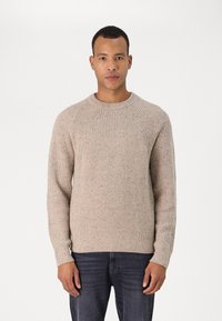 Beige knitted sweater with a crew neckline and ribbed texture. Features raglan sleeves and a straight hem. Worn with dark denim jeans.