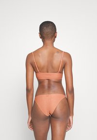 Dvoudielny bikiny v matnej terakotovej farbe, s tenkými popruhmi, s rebrovanou textúrou a minimalistickým dizajnom pre vrchnú a spodnú časť.
