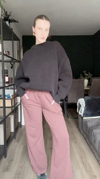 Suéter negro de punto de gran tamaño con cuello acanalado, combinado con pantalones de pierna ancha en rosa claro que incluyen bolsillos y un cordón ajustable.