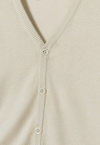 Cardigan beige clair avec un col en V, bordures côtelées et quatre boutons assortis sur le devant. Matière en tricot douce avec une texture lisse.