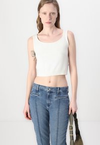 Top corto bianco realizzato in tessuto a coste, abbinato a jeans slim-fit blu in denim con tasche frontali e cuciture sottili.