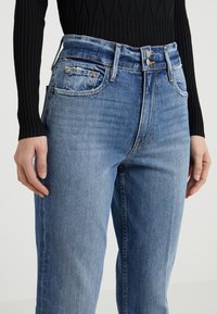 Ljusblå denimjeans med hög midja, utrustade med en knappstängning med två knappar, synliga framfickor och en något blekt textur.