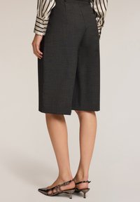 Tummanharmaat räätälöidyt shortsit, joissa on suora leikkaus ja teksturoitu kangas, on yhdistetty kuvioituihin ja raidallisiin hihoihin sekä korkokenkiin.