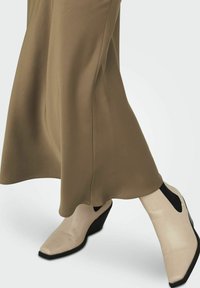Bottes compensées beiges à bout pointu, avec des accents latéraux noirs et une finition texturée, assorties à une jupe fluide vert olive.