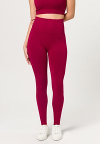 Strakke, hoge taille leggings in levendig magenta, gemaakt van een zachte, rekbare stof. Gecombineerd met een bijpassende crop top en witte sneakers.