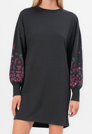 Sort kjole med lange ærmer og puffede ærmer med pink og grøn blomsterbroderi på underarmene, rund halsudskæring, båret af en person fra halsen til midt på låret.