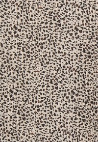 Tissu beige présentant un motif léopard avec des taches brun foncé et noires, surface texturée avec des rayures verticales.