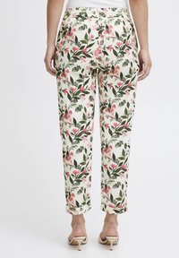 Pantalon à imprimé floral en crème avec des fleurs roses et des feuilles vertes. Coupe décontractée et taille élastique. Ourlet légèrement retourné.