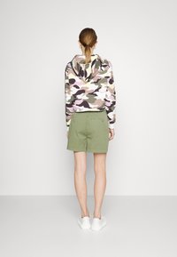 Kort hættetrøje med camouflageprint i pink, grøn og hvid med snøre i hætten, parret med olivengrønne shorts og hvide sneakers.