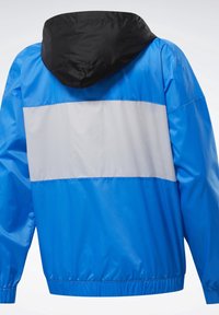 Veste coupe-vent bleue avec une large bande réfléchissante grise horizontale sur le dos et une capuche noire.