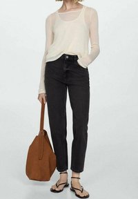 Jasnobeżowa bluzka z długim rękawem, czarne dżinsy z wysokim stanem, brązowa zamszowa torba i czarne płaskie sandały. Strój ma swobodną, warstwową estetykę.