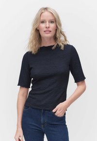 Marinblå texturerad kortärmad topp med rund halsringning, kombinerad med blå jeans. Tyget har ett subtilt veckmönster och en avslappnad passform.