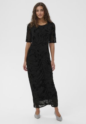 Black velvet dress with floral texture, short sleeves, and a draped design. Paired with light gray heeled shoes.