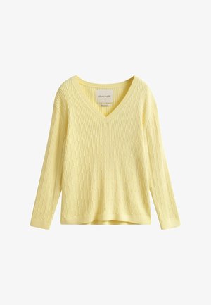 Pull jaune pâle à manches longues avec col en V, texture côtelée et torsadée, étiqueté "GANT", présenté sur un fond blanc.