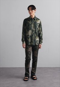 Green floral-patterned shirt and matching pants made of smooth fabric, paired with black sandals. Casual, coordinated outfit.