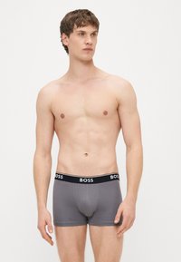 Cuecas boxer cinzentas com cintura elástica preta que apresenta o nome da marca "BOSS" em branco. Material macio com um design ajustado.