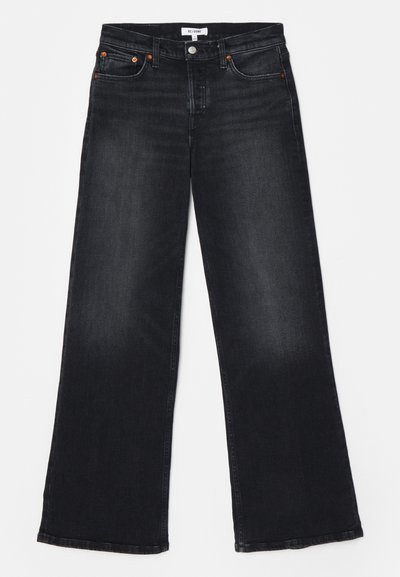 Jeans en denim noir taille haute avec une coupe large, cinq poches, des coutures orange et une texture légèrement déchirée.