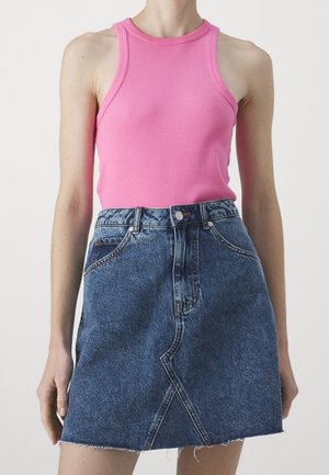 Vrouw draagt een mouwloze roze geribbelde tanktop die is ingestopt in een high-waisted blauwe denim rok met een voornaad en een ruwe zoom.