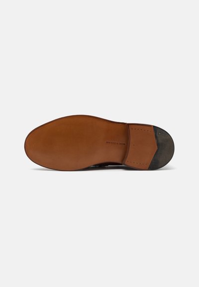 Suola di scarpa in pelle marrone con una superficie liscia, forma arrotondata e tacco leggermente usurato; il dettaglio stampato riporta "Made in England."