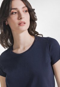 Granatowy t-shirt z krótkim rękawem i okrągłym dekoltem. Tkanina wydaje się gładka i lekka. Brak widocznych wzorów lub ozdób.