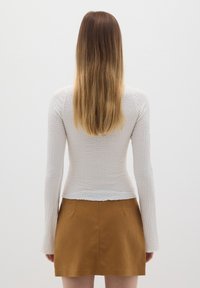 Top blanco texturizado de manga larga con silueta ajustada, combinado con una mini falda de ante marrón con un acabado suave y un ligero brillo.